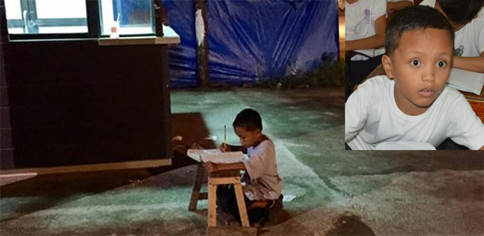 Homeless nine-year-old boy Daniel Cabrera doing his homework on a wooden stool placed close to a fastfood restaurant