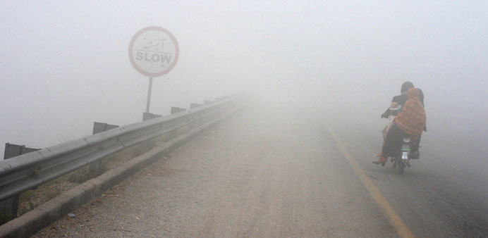 A Pakistani family rides on a motorbike along a road during a foggy day in Peshawar on December 19.