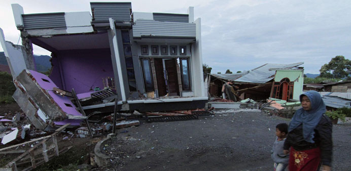An Acehnese woman and a child walk past damaged houses in Blang Mancung yesterday following an earthquake on Tuesday.