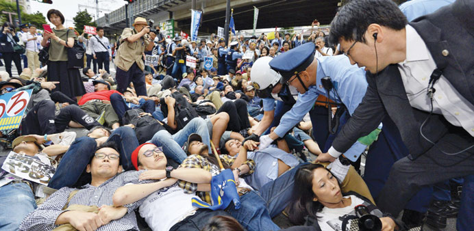 Protesters lie on the ground as they try to stop a car carrying members of the parliamentu2019s upper house security bills committee in Yokohama, south of