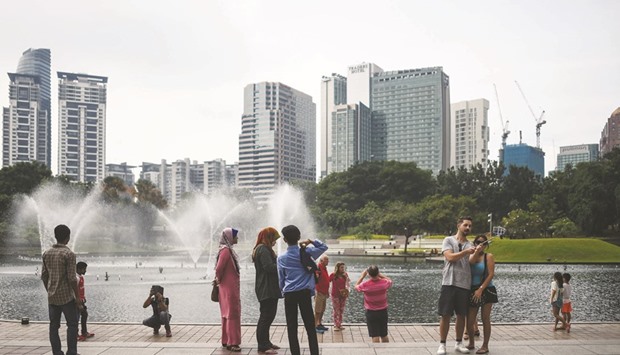 Tourists take pictures in a park in Kuala Lumpur. Malaysiau2019s economic growth eased in the second quarter, the central bank said yesterday, attributing the slowdown to a decline in exports amid subdued global demand.