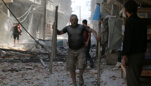 A Syrian man covered with dust carries pieces of metal on a street cluttered with rubble following a reported air strike on the rebel-held neighbourhood of Sakhur in the northern city of Aleppo, on August 15, 2016