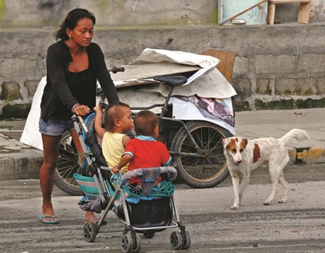 A woman pushes her children on a stroller after around a dozen homeless people were evicted along a road in Makati, Metro Manila, yesterday.