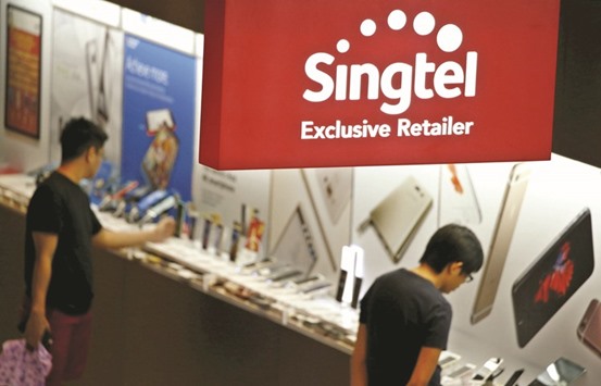 People look at mobile handsets at a SingTel retailer shop in Singapore. The telecom firm will acquire 21% of Thailandu2019s Intouch and an additional 7.39% in Indiau2019s Bharti Telecom from state-linked investment company Temasek.