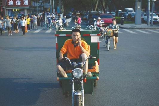 A Chinese delivery courier using a mobile phone as he drives his delivery vehicle across a street in Beijing.