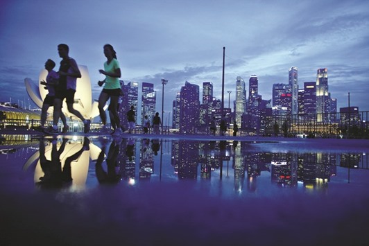 Joggers run past as the skyline of Singaporeu2019s financial district is seen in the background. The city-stateu2019s private banks are coming under scrutiny for earning bonuses by selling risky debt, as the city sees an unprecedented wave of defaults. The central bank says an industry group is reviewing the practice.