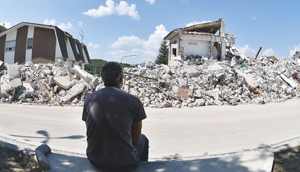 A man sits yesterday in front of collapsed houses in Amatrice.