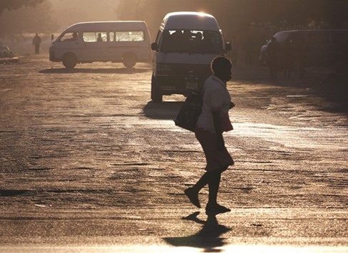 A woman crosses the street in front of minibus taxis in Harare.