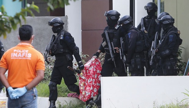 Indonesian anti-terror police personnel carry a bag containing a suspected firearm and other evidence from a building during a raid in Batam.