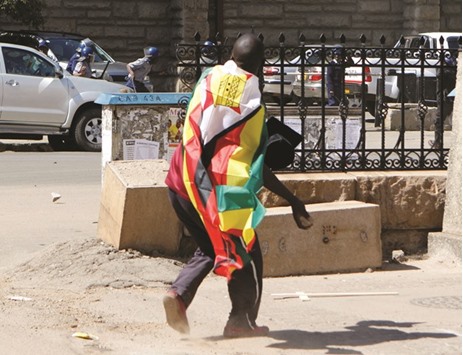 A man wrapped in a Zimbabwean flag throws stones at police officers during a protest in Harare on Wednesday against President Robert Mugabeu2019s governmentu2019s handling of the economy.