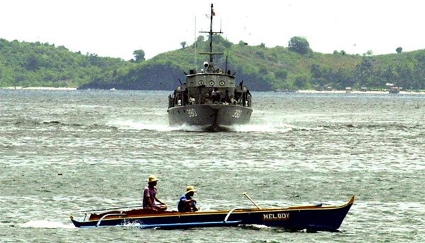 A navy cutter patrols the shores of a fishing village near the capital town of Jolo of Sulu as an outrigger races across its path
