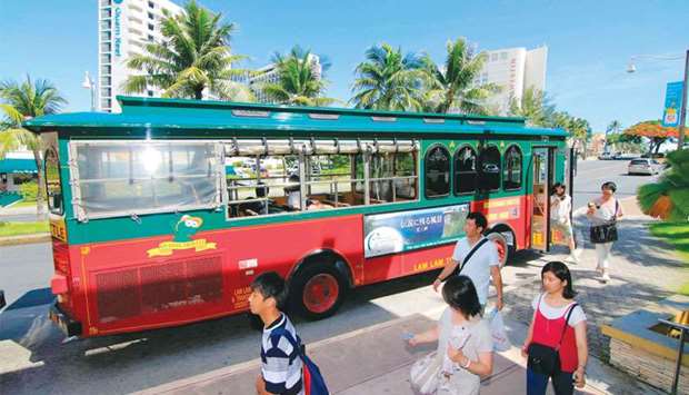 Tourists disembark from a bus along a street in Tamuning.