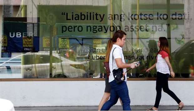 People walk past an Uber advertisement outside the Uber main office in Mandaluyong city, Metro Manila, on Tuesday.