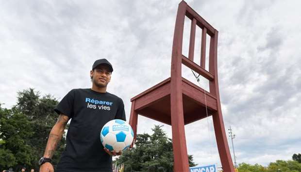 Brazilian superstar Neymar poses next to the monumental wood sculpture ,Broken Chair, during an event organized by NGO Handicap International 