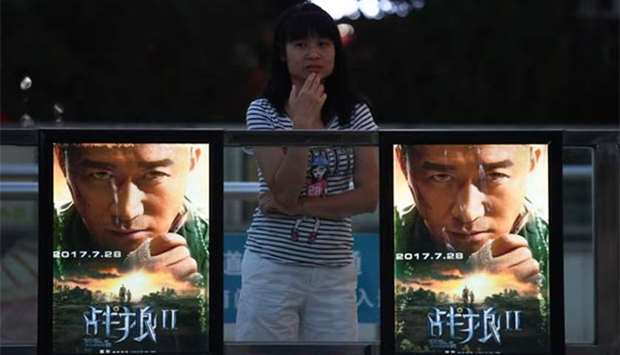 A woman stands next to a movie poster for ,Wolf Warriors 2, in Beijing.