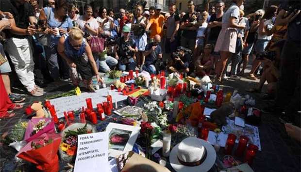 People stand next to flowers, candles and signs set up on the Las Ramblas boulevard in Barcelona as they pay tribute to the victims of the Barcelona attack, on Friday.