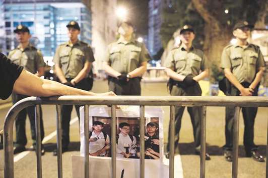 A protester holds a photo of jailed Hong Kong student leaders Joshua Wong, Nathan Law and Alex Chow, while officers from the Correctional Services Department standing guard outside a prison in Hong Kong, China.