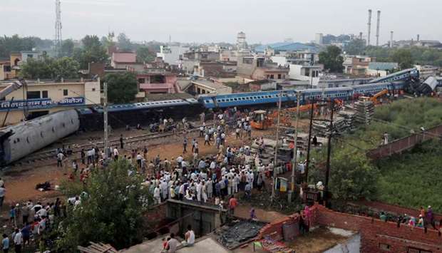 Rescue workers and onlookers stand next to derailed coaches of a passenger train in Khatauli