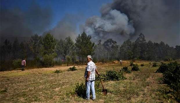 A man stands holding a shovel as a wildfire approaches the city of Macao in Portugal this week.