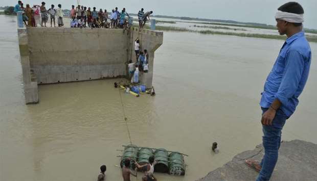 Villagers attempting to cross flood waters with the help of rope and empty canisters next to a washed away portion of a bridge