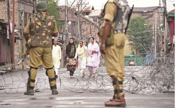 Paramilitary troopers stand guard as pedestrians walk along a road during restrictions after Kashmiri separatists called for a one-day strike to protest a civilian killing in Srinagar yesterday.