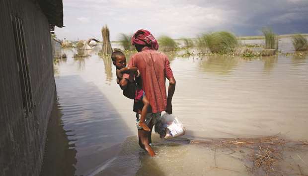 A man with a child walks along a flooded area as he returns home from market in Gaibandha, Bangladesh.