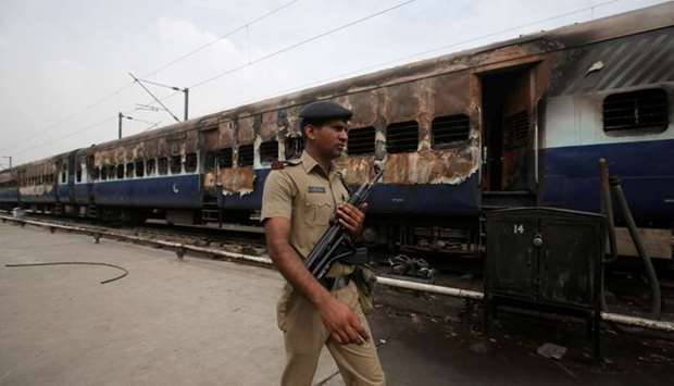 A security personnel member walks past a burnt carriage of a train near a railway station in New Delhi, India