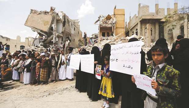 Yemenis stand in protest yesterday amidst the debris of a house, hit in an air strike on a residential district, in the capital Sanaa.