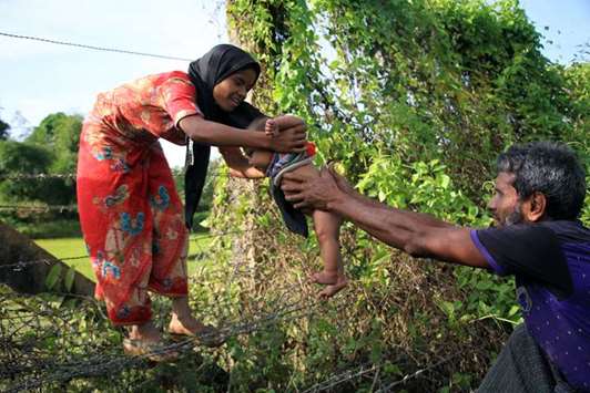 A Rohingya man passes a child through a barbed wire border fence near Maungdaw yesterday.