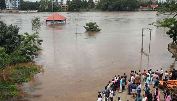People stand on the steps of Aluva Shiva Temple complex submerged in water after the opening of Idamalayar dam shutter following heavy rains, on the outskirts of Kochi, on Thursday.