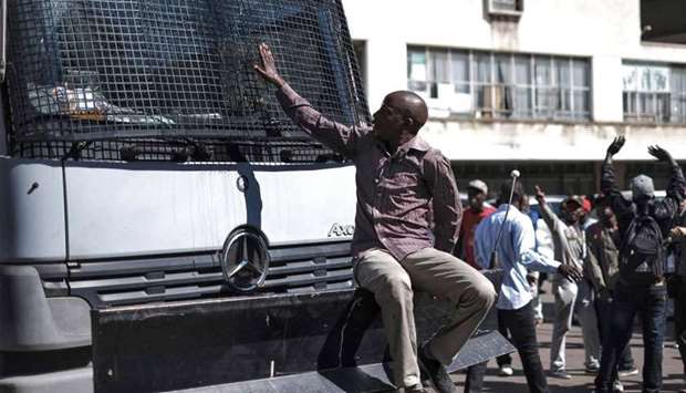 A supporter of Zimbabwean opposition MDC Alliance party sits in front of the bonnet of an anti-riot police truck as other supporters react outside the MDC Alliance's headquarters in Harare