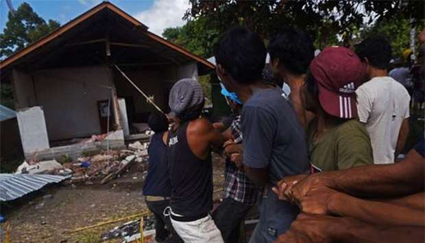 Residents pull down a house damaged by earthquake in Kayangan, North Lombok.