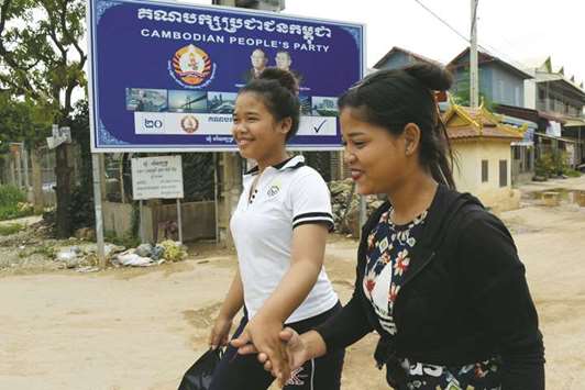 Women walk past the billboard of the ruling Cambodian Peopleu2019s Party bearing the portraits of Cambodiau2019s strongman Premier Hun Sen and National Assembly President Heng Samrin in Kandal.