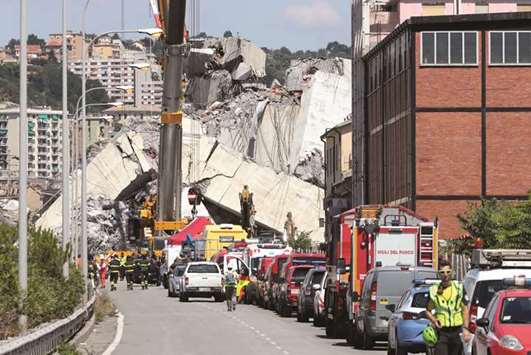 Firefighters and rescue workers stand at the site of a collapsed Morandi Bridge in the port city of Genoa.