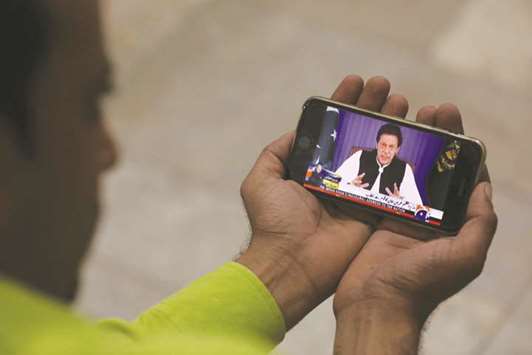 A journalist in Karachi poses with a cellphone displaying Imran Khan speaking to the nation in his first televised address.