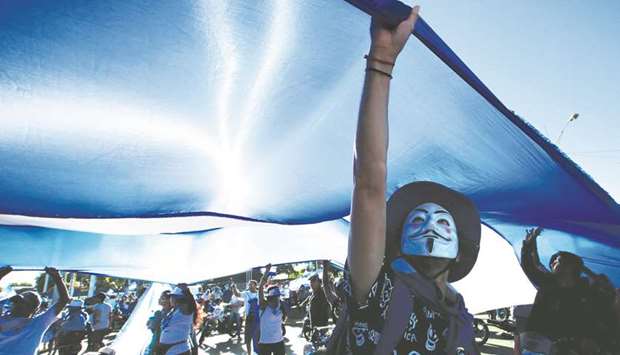 A masked demonstrator holds a big national flag during a protest against Nicaraguan President Daniel Ortegau2019s government in Managua, Nicaragua.