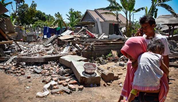 A woman carries her child as they make their way pass collapsed homes in the village of Sugar on Indonesia's Lombok island.
