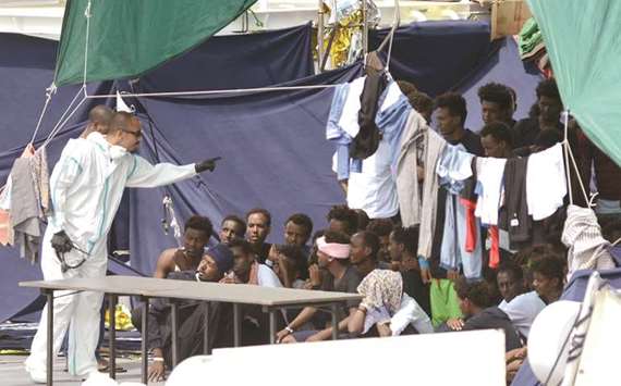 An official wearing a protective suit gestures towards migrants on the deck of the Italian Coast Guard vessel u2018Diciottiu2019, in the Sicilian port of Catania.