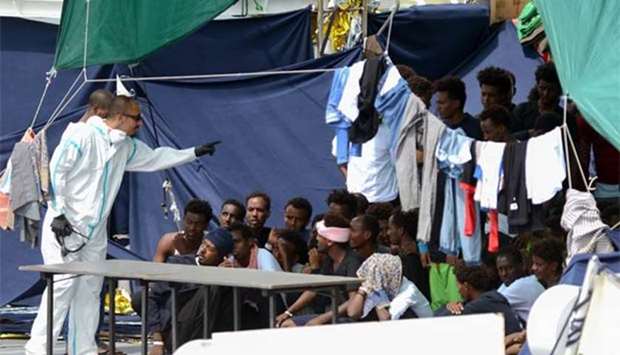 An official wearing a protective suit gestures towards migrants as they sit on the deck of the Italian Coast Guard vessel Diciotti in the Sicilian port of Catania on Thursday.