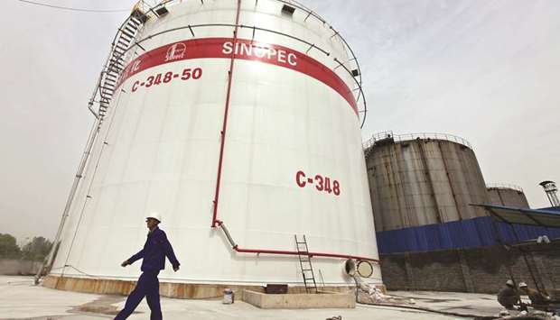 An employee walks past oil tanks at a Sinopec refinery in Wuhan, Hubei province, China (file). Net income for the company for the first half was 41.6bn yuan ($6.05bn), rising 53.6% from a year ago.