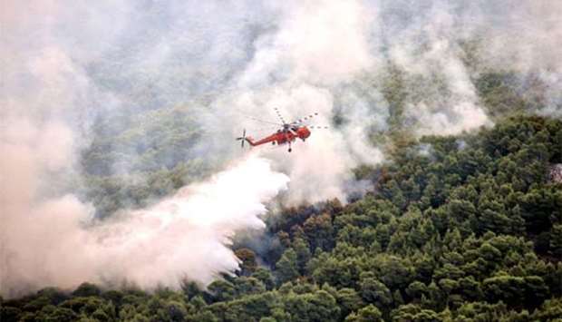 A firefighting helicopter drops water to extinguish flames during a wildfire at the village of Kineta, near Athens, on July 25, 2018.