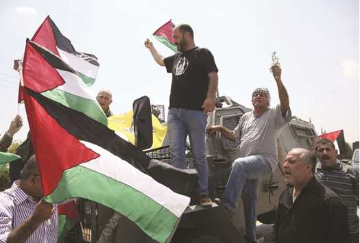 Protesters from the occupied West Bank village of Bardala and their supporters raise flags and an olive branch as they prevent an Israeli military vehicle from driving on a road during a protest against water shortage in the area, yesterday.