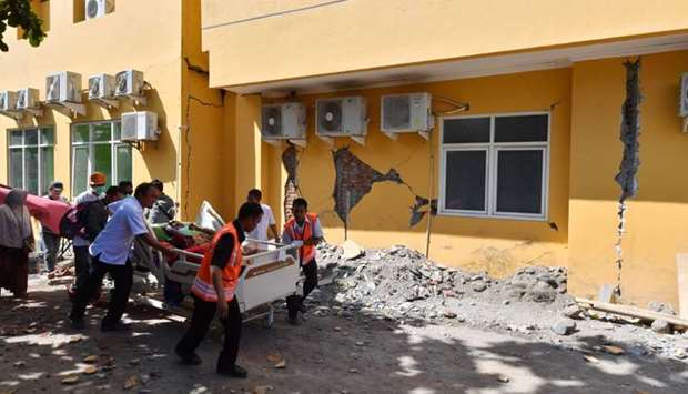 A man is wheeled passed a damaged wall to a makeshift ward set up outside the Moh. Ruslan hospital in Mataram on the Indonesian island of Lombok.