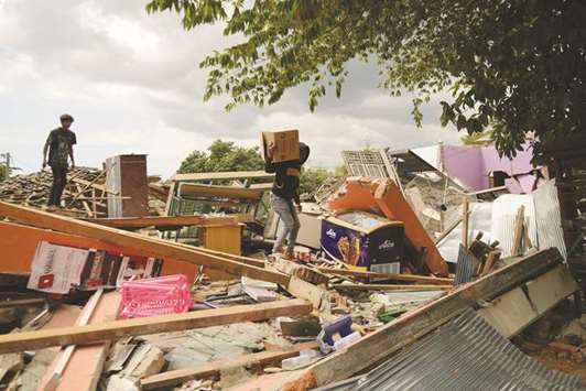 A young man salvages belongings as he climbs over debris of a collapsed house in Kayangan in northern Lombok island yesterday.