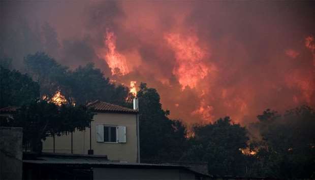 Flames rise next to a house as a wildfire burns at the village of Kontodespoti, on the island of Evi