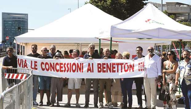 People hold a banner as they demonstrate during ceremonies marking the first anniversary of the collapse of a motorway Morandi Bridge that killed 43 people in Genoa. The banner reads: u201cOut with concession for Benettonu201d.