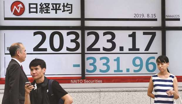 Pedestrians stand in front of an electronic quotation board displaying the numbers on the Nikkei 225 index at the Tokyo Stock Exchange.