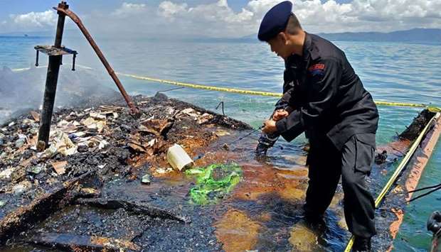 Indonesian policeman inspecting the charred remains of a ferry that caught fire near Kendari, off Indonesia's Sulawesi island