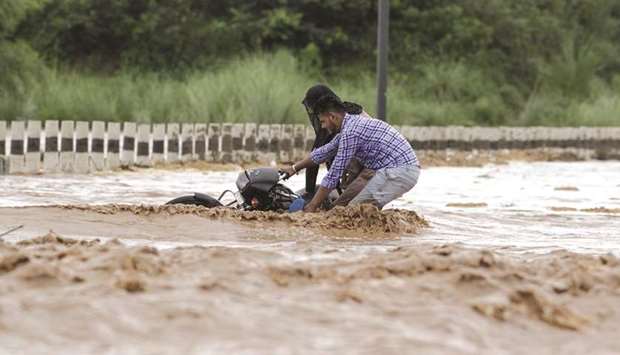 Two men try to handle their motorbike as they wade through a flooded water channel flowing over a bridge after heavy rains at New Chandigarh in Mohali district in Punjab yesterday.