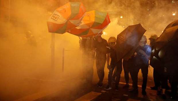 Pro-democracy protesters shield themselves with umbrellas in tear gas as they clash with police in Hong Kong yesterday